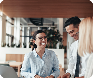 Three colleagues engaged in a lively conversation in a modern office, reflecting a collaborative and positive work environment with a bright, open space and plants