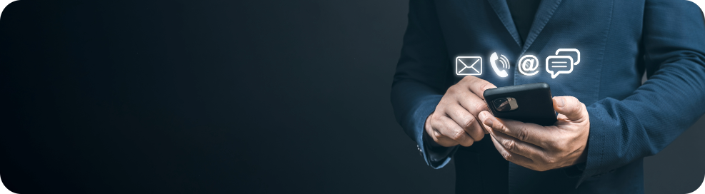 The image features a person dressed in a dark suit, holding a smartphone with both hands. Floating icons near the phone represent various communication methods, including an envelope for email, a phone symbol, an '@' symbol for email or web, and a speech bubble for messaging or chat. The background is a dark gradient, giving the scene a professional and modern feel, suggesting a focus on digital or business communication.